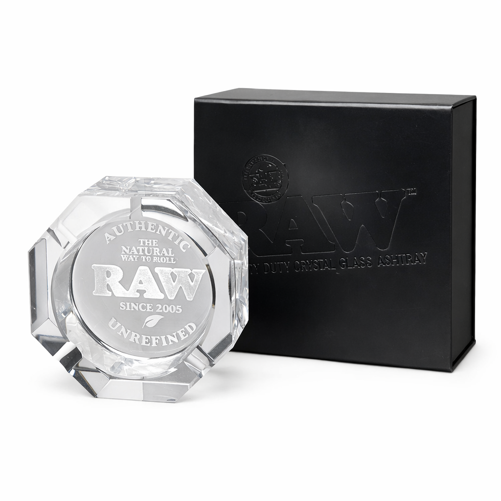 Clear glass ashtray with 'RAW' branding next to a black box on a white background
